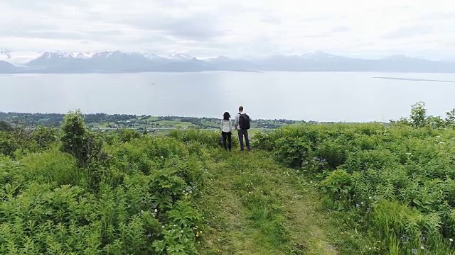 高清4K航拍:一对年轻的异族情侣在完成徒步旅行后欣赏阿拉斯加多山的海岸线美景视频下载
