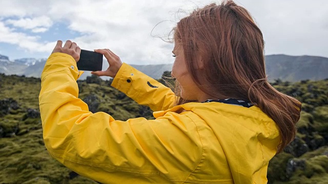 身穿黄色雨衣的游客在火山景观上拍摄苔藓视频素材