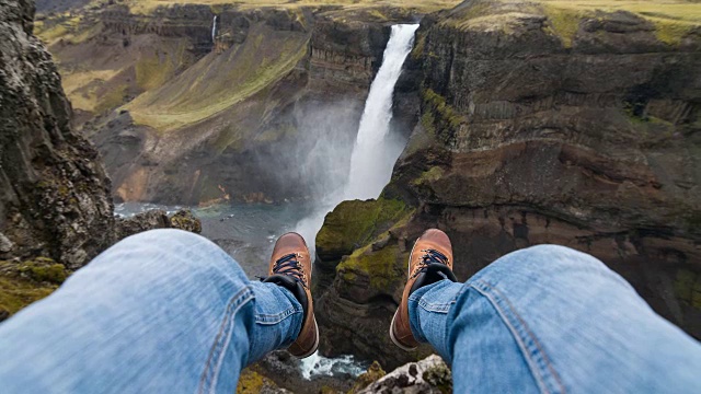 一个人坐在悬崖上，看着峡谷里的瀑布视频素材