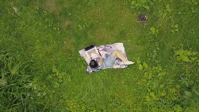 无人机拍摄的年轻女子在草地上用笔记本电脑工作视频下载