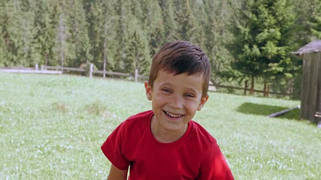 微笑可爱的男孩做有趣的手势，而坐在篱笆在山上视频素材