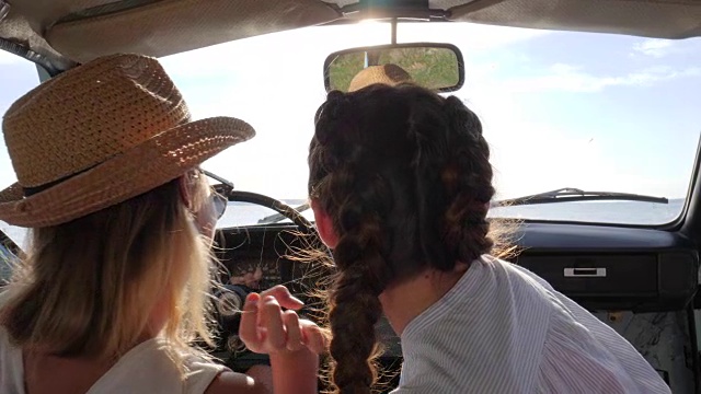 坐在汽车前排的女孩们在天际线上谈笑，看着远方，可爱的女友们快乐的旅程视频素材