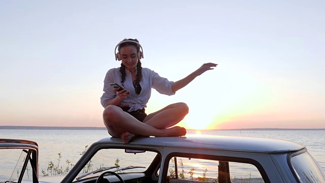 快乐的旅程，夏日海滨休息的乐趣，女孩在河岸边的车顶上欣赏音乐视频素材