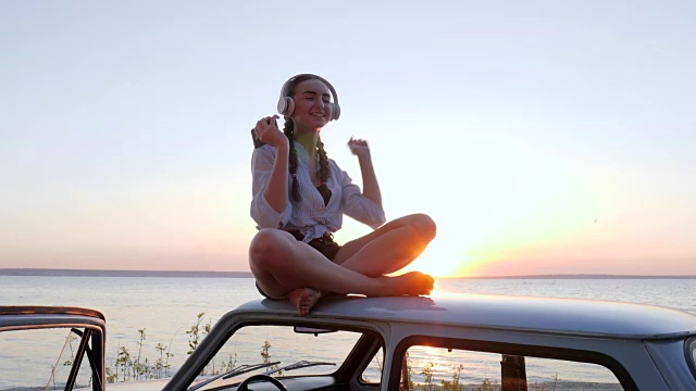 女孩戴着蓝牙耳机在河堤上听歌，背景是日落，夏日休息的乐趣，背光视频素材