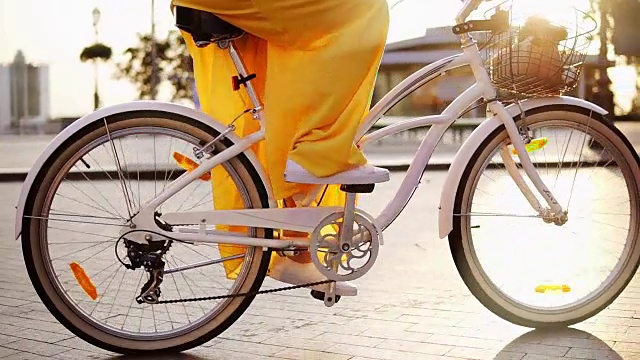 一个白色城市自行车的轮子旋转的特写。有铃铛，篮子和花的城市自行车。清晨，一个面目全非的女人骑着一辆城市自行车。替身。Slowmotion视频素材