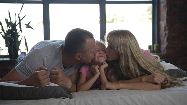 慈爱的父母亲吻躺在床上的女儿视频素材