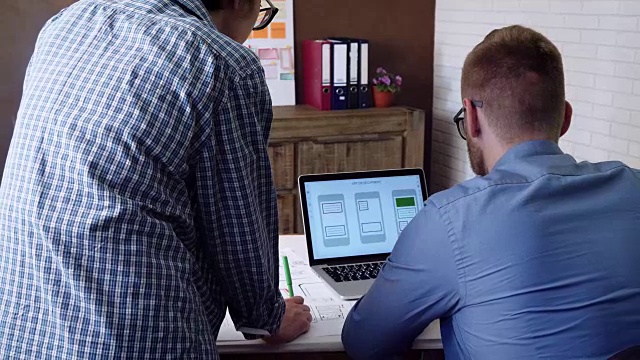 移动应用程序开发人员草图设计的新应用程序和他的同事看他的工作视频素材