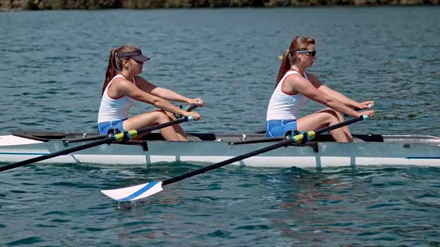 在一个阳光明媚的日子里，两名女运动员划着桨横渡湖面视频素材