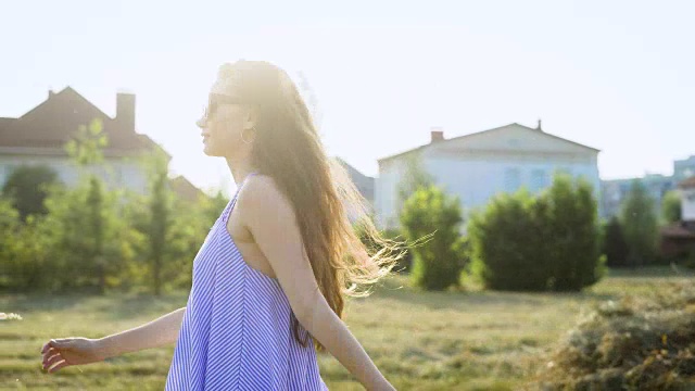 一个快乐的棕色头发的女人正戴着太阳镜走在阳光明媚的夏日里视频素材