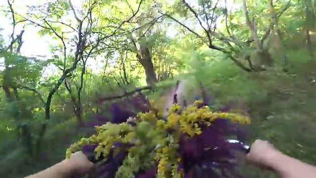 女孩骑着自行车在森林小径上，手里拿着一束花视频素材