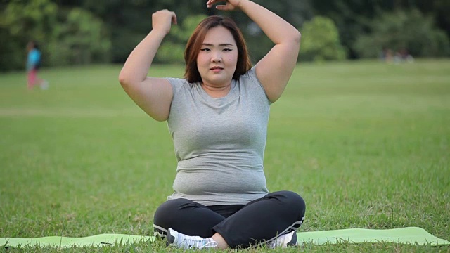 在公园的草地上练习瑜伽的大号亚洲女人视频下载