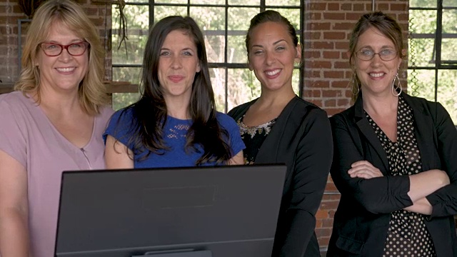 四个自信成功的商业女性微笑在电脑显示器后面视频素材