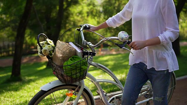 特写的女人的手拿着一个城市自行车的车把与鲜花和书的篮子。在城市公园里享受时光的女人。夏季视频素材