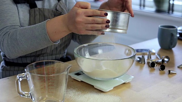 特写的年轻女子手筛面粉在碗。金发女性正在称量烹饪原料视频素材