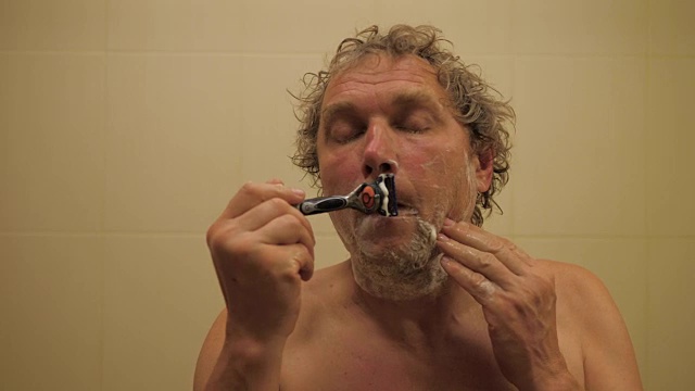 在浴盆里用剃刀刮胡子的男人。视频下载