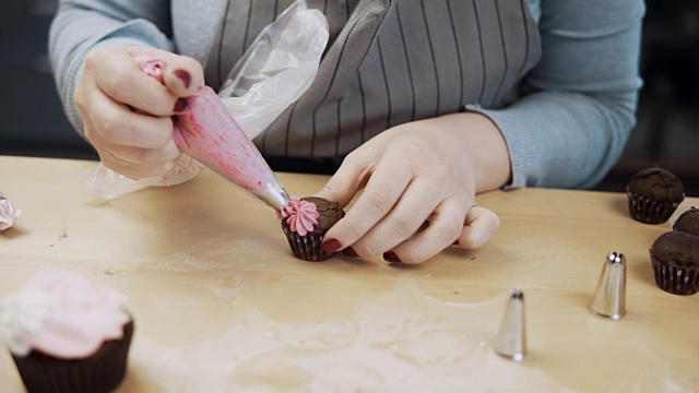 近距离观察女性的手装饰的巧克力纸杯蛋糕与粉色奶油，使用糕点袋视频素材