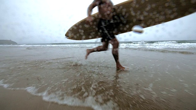 一个成熟的男性冲浪者在海边奔跑。视频素材