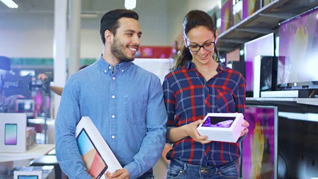 一对幸福的夫妇在电子商店里散步，他们为他买了最新款的平板电脑，为她买了新的智能手机。购物中心大，明亮，充满了最新的电子产品。视频下载