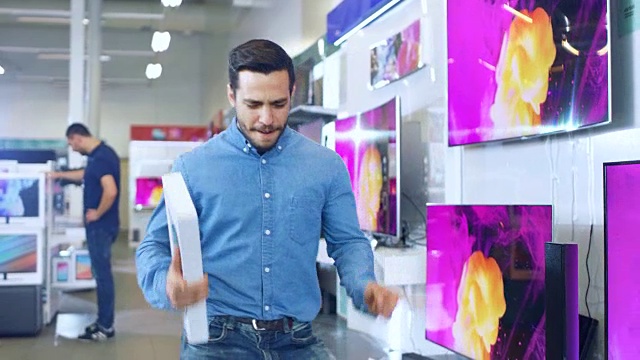 一名年轻人在电子商店购买了最新款的平板电脑，并高兴地与盒子跳舞。明亮和现代商店有所有最新的设备在商店。视频下载