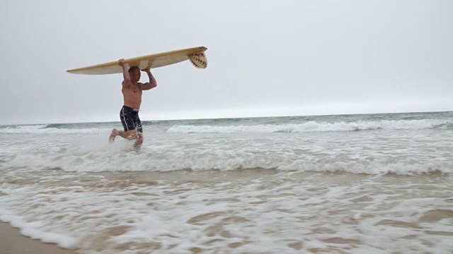 一个中年冲浪者带着他的长板在海浪中冲浪。视频素材