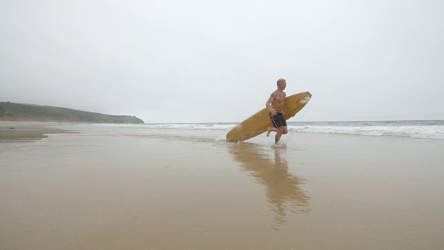 一个成熟的男性冲浪者正带着他的长板冲进海浪中。视频素材