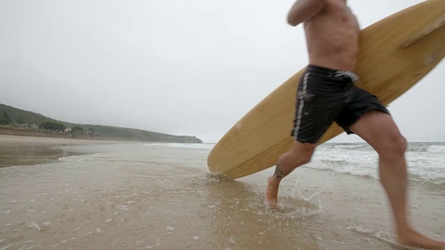 一个中年冲浪者在慢镜头中奔向大海。视频素材