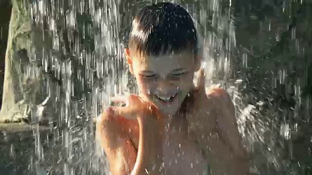 小男孩在喷泉下的水池里跳舞，在炎热的夏日里得到了极大的快乐视频素材