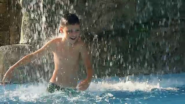 小男孩在喷泉下的水池里跳舞，在炎热的夏日里，在露天里获得极大的快乐视频素材