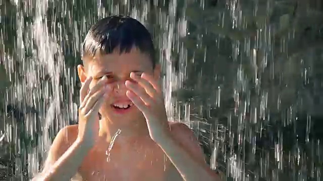 小男孩在喷泉下的水池里跳舞，在炎热的夏日里，心情舒畅，不愿离开水的清凉视频素材