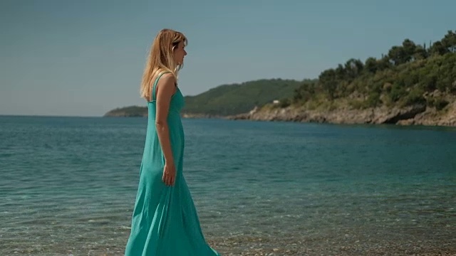 一个穿着天蓝色长裙的女人独自在海滩上散步视频素材