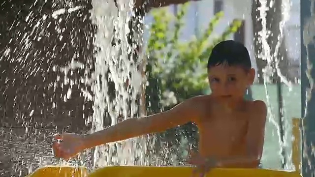 小男孩高兴地站在水上公园的小溪瀑布下视频素材