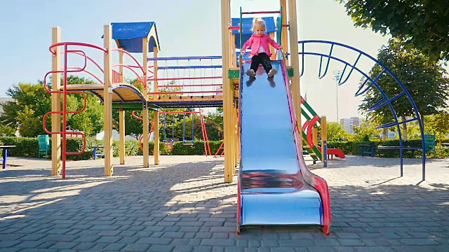慢镜头:一个三岁的女孩从公园操场上的滑梯上下来。视频素材