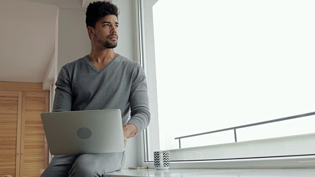 非裔美国人坐在窗边，用笔记本电脑上网。视频素材