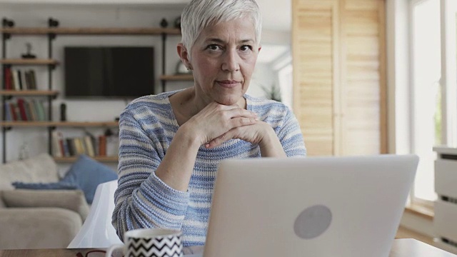 成熟的女人坐在家里用笔记本电脑上网。视频素材