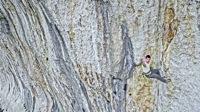 一名男性攀岩者对着镜头挥手，然后从悬崖上下来视频素材
