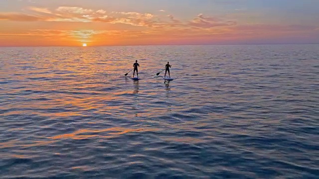 空中男人和女人在日落时划着他们的sup视频下载