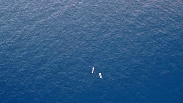 上方是两个人划着他们的sup在平静的蓝色海面上视频下载