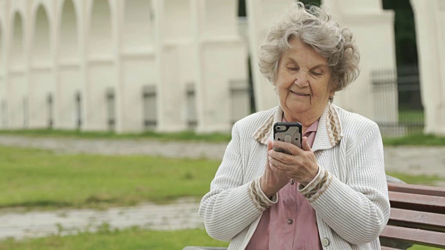 一个成熟的老妇人在户外拿着银色的智能手机视频素材