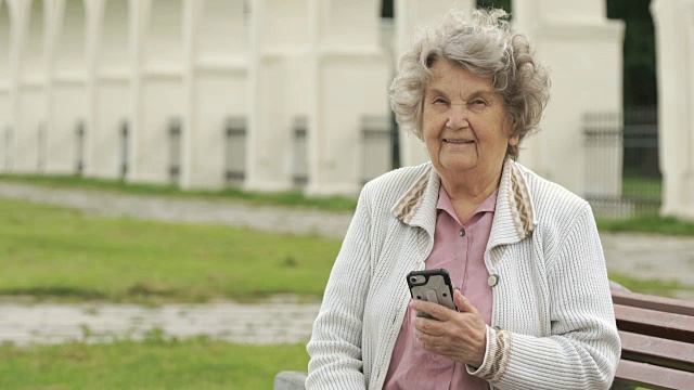 一位老年妇女在户外手持银色智能手机视频素材