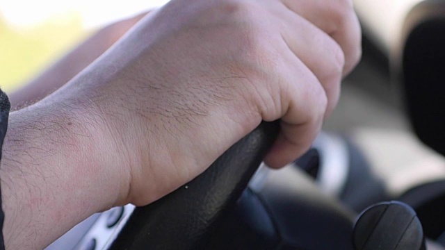 慢镜头拍摄的男子双手放在汽车方向盘上，男子正在城市里开车。1920 x1080视频下载