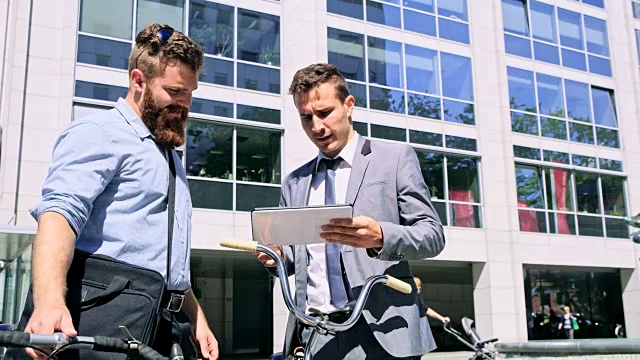 两个商人骑着自行车在城市里使用数字平板电脑视频素材