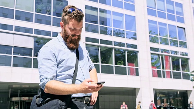 DS潮人穿着衬衫在办公大楼前使用智能手机视频素材