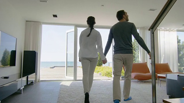 幸福的年轻夫妇手牵着手，非常爱跑出他们的家到阳台与海边的景色。视频下载