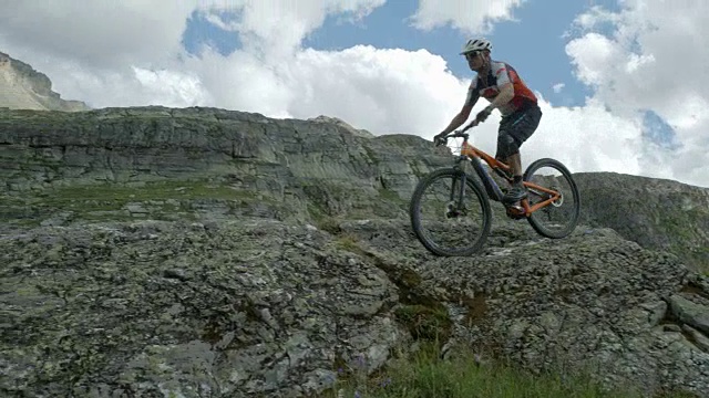 一名50-59岁的成熟男性山地摩托车手骑在多岩石的山地上。视频素材