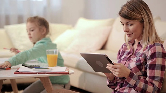 微笑的女人用着平板电脑，背景是她的女儿。视频素材