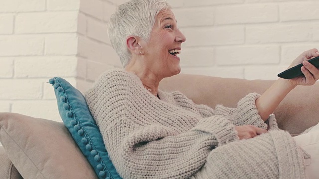 快乐成熟的女人一边看电视一边放松在家的沙发上。视频素材