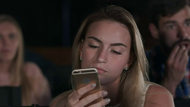 一位年轻漂亮的女性在当地电影院看电影时发短信视频素材