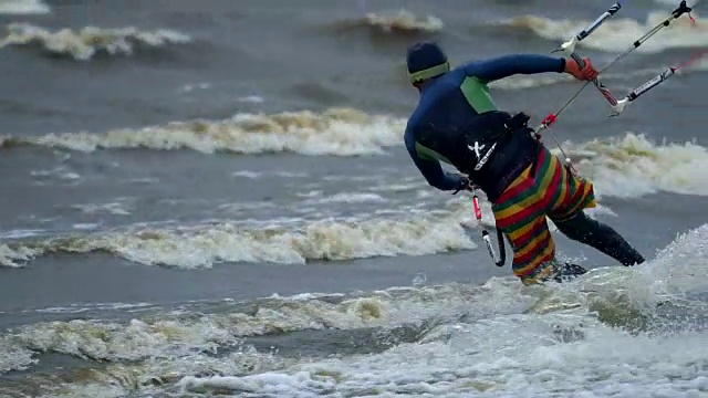 慢镜头:一个年轻人正在放风筝。他在滑板上在池塘的波浪上漂亮地滑着。强烈的风。人们喜欢在极端天气下放风筝。寒冷的秋天的天气视频下载