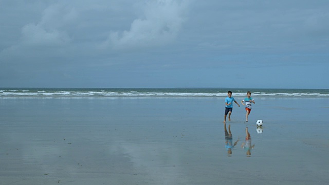 两个小男孩笑着玩沙滩足球的慢镜头。视频素材
