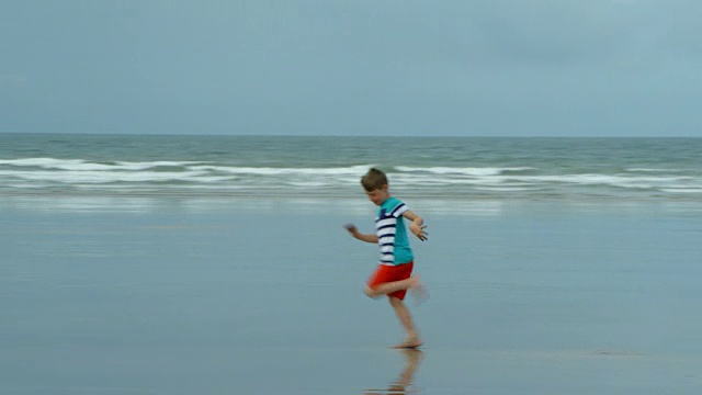 一个在沙滩上跑步的小男孩回头看了看他在沙滩上的脚印。视频素材